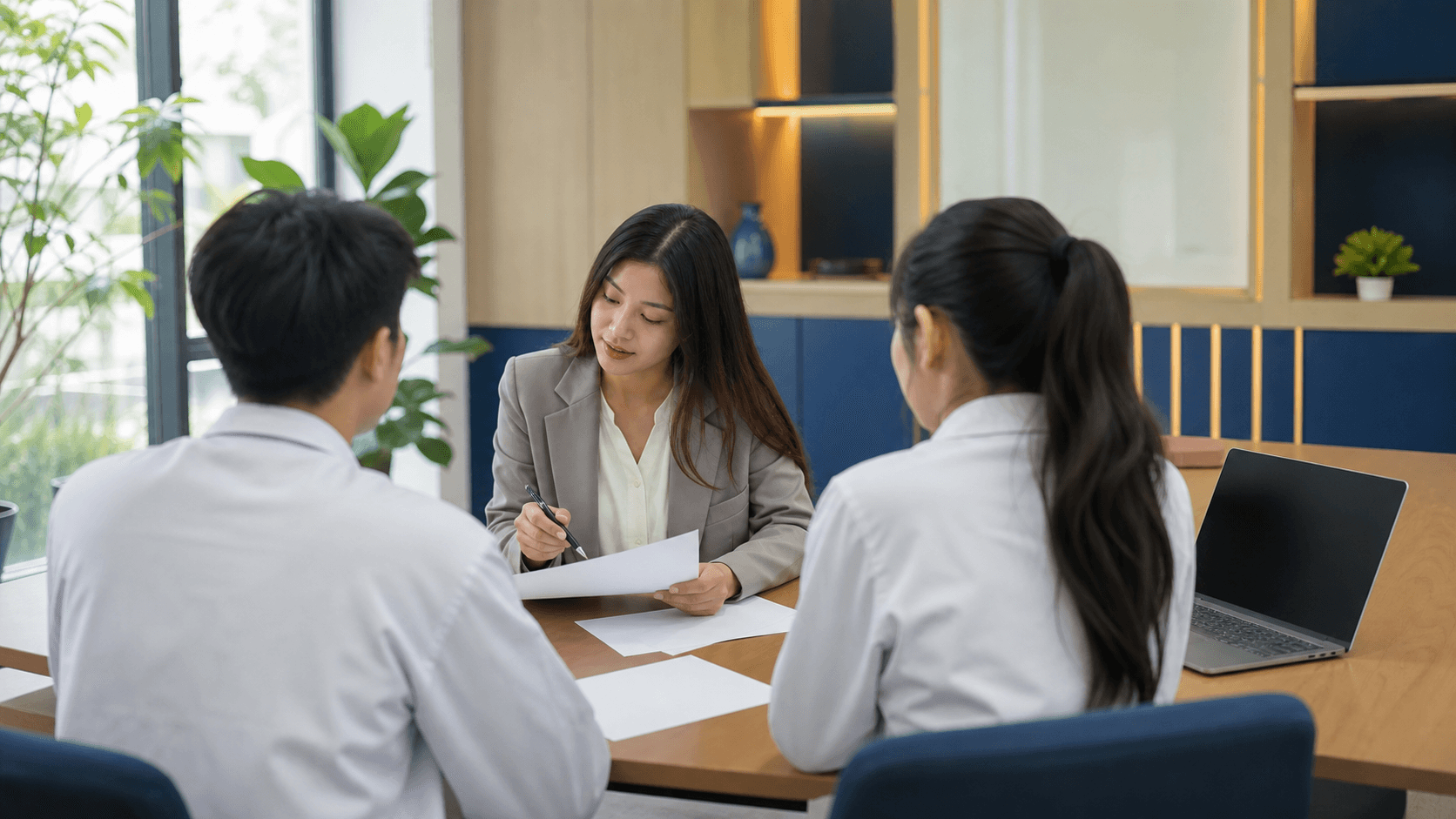 Non-identifiable medical students discussing blank papers with a student-support adviser in an unbranded Vietnamese university room